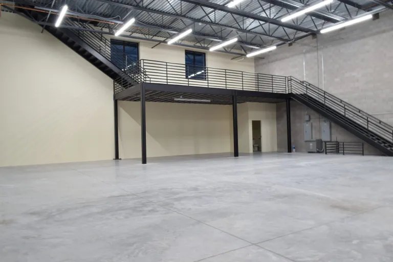 Empty unit at The Stack Auto Lofts with a steel mezzanine and stairs along the back wall