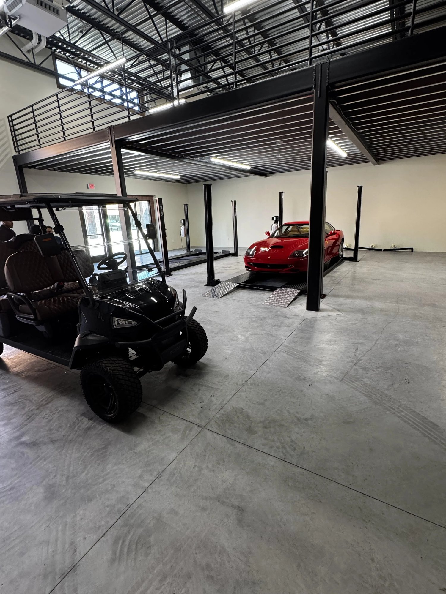 Finished unit at The Stack Auto Lofts with a red Ferrari on a lift and a golf cart parked under the mezzanine